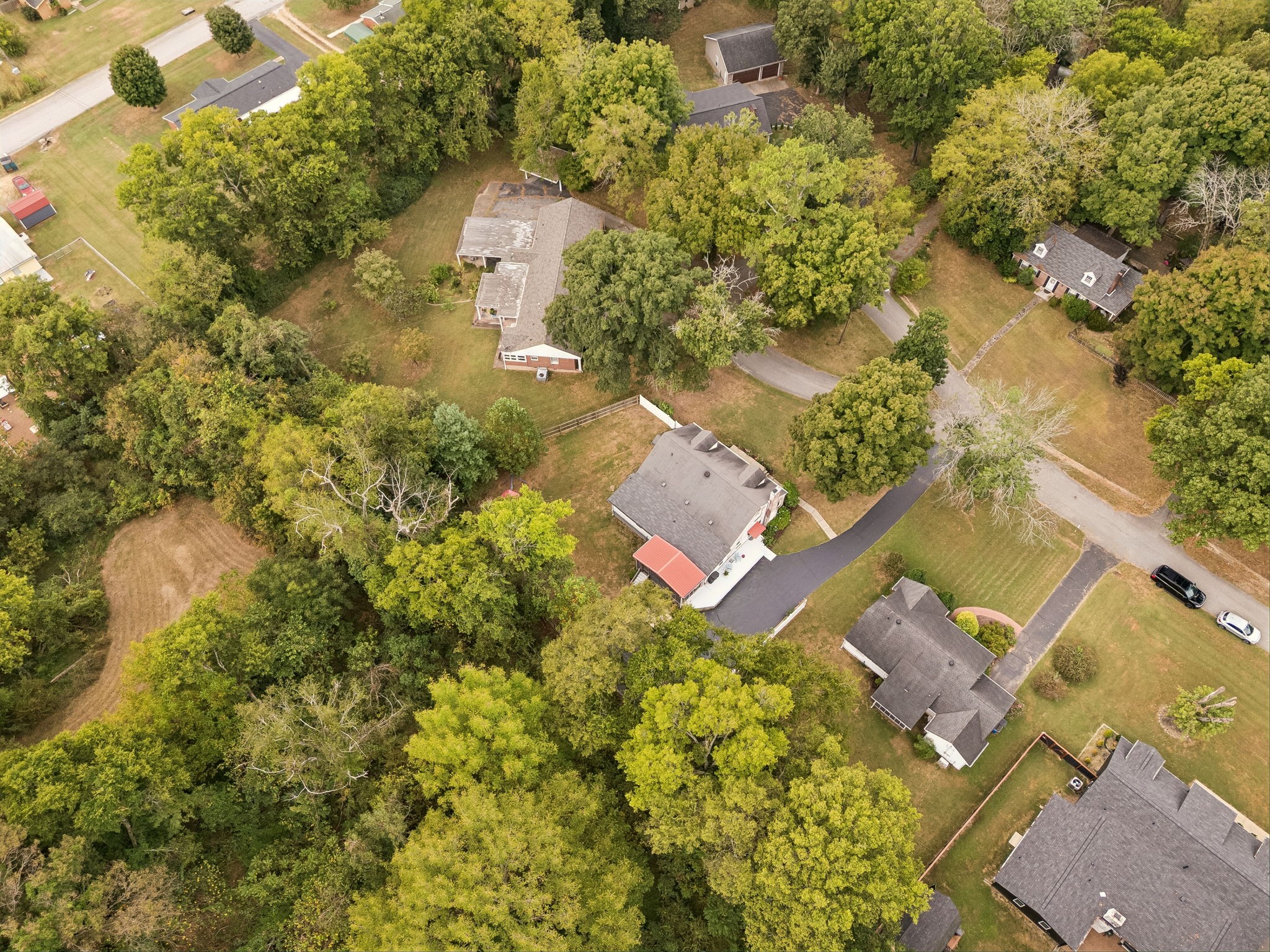 Aerial view of a wooded home and curved driveway among neighboring houses.