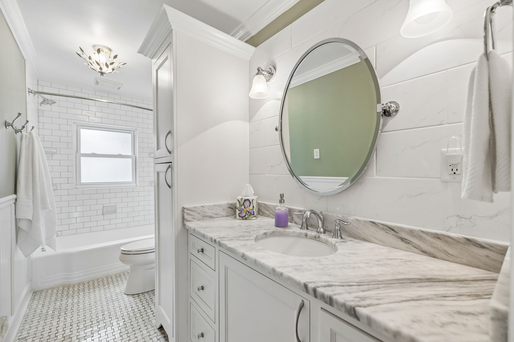 Bathroom with a marble vanity, oval mirror, and bathtub with white subway-tile surround.