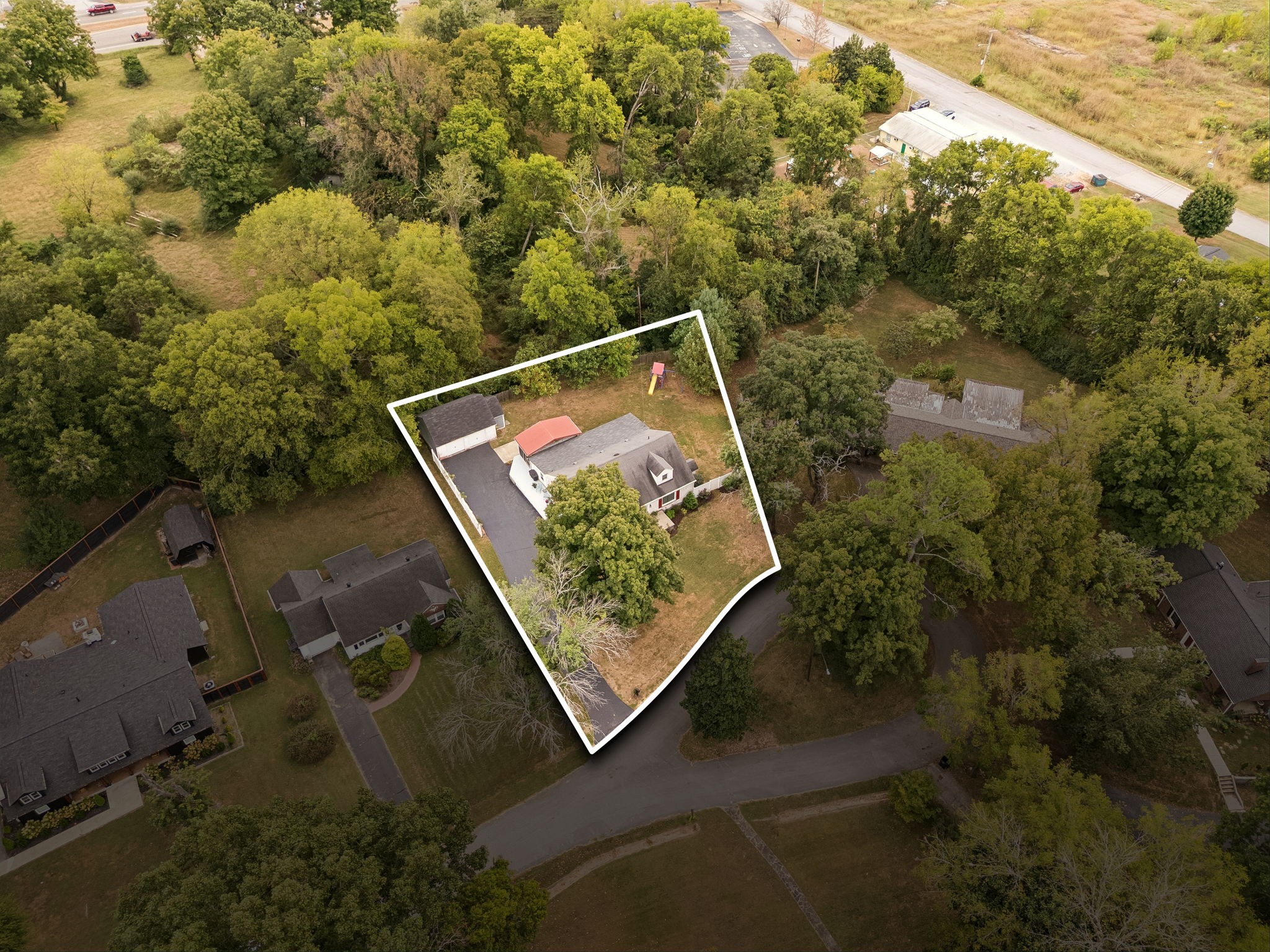 Aerial view of a wooded property outlined in white, with a home, outbuildings, and paved driveway.