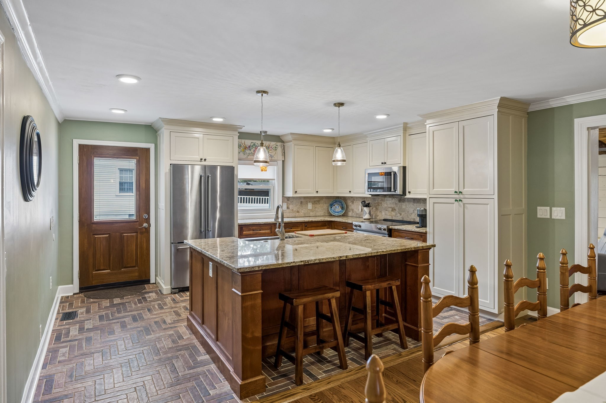 Kitchen with a granite island, cream cabinets, stainless appliances, and patterned tile flooring.
