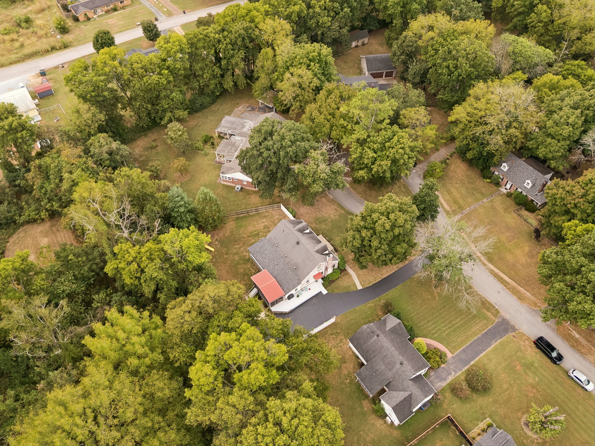 Aerial view of a home with a curved driveway, red awning, and mature trees.
