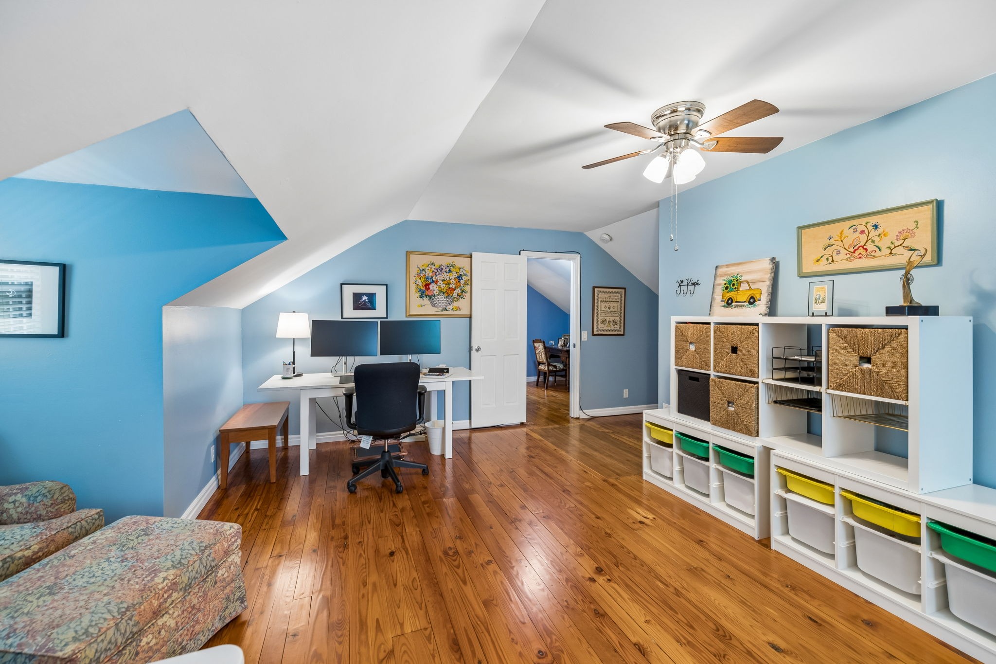 Attic home office with blue walls, wood floors, a desk, and white cubby shelving with baskets.
