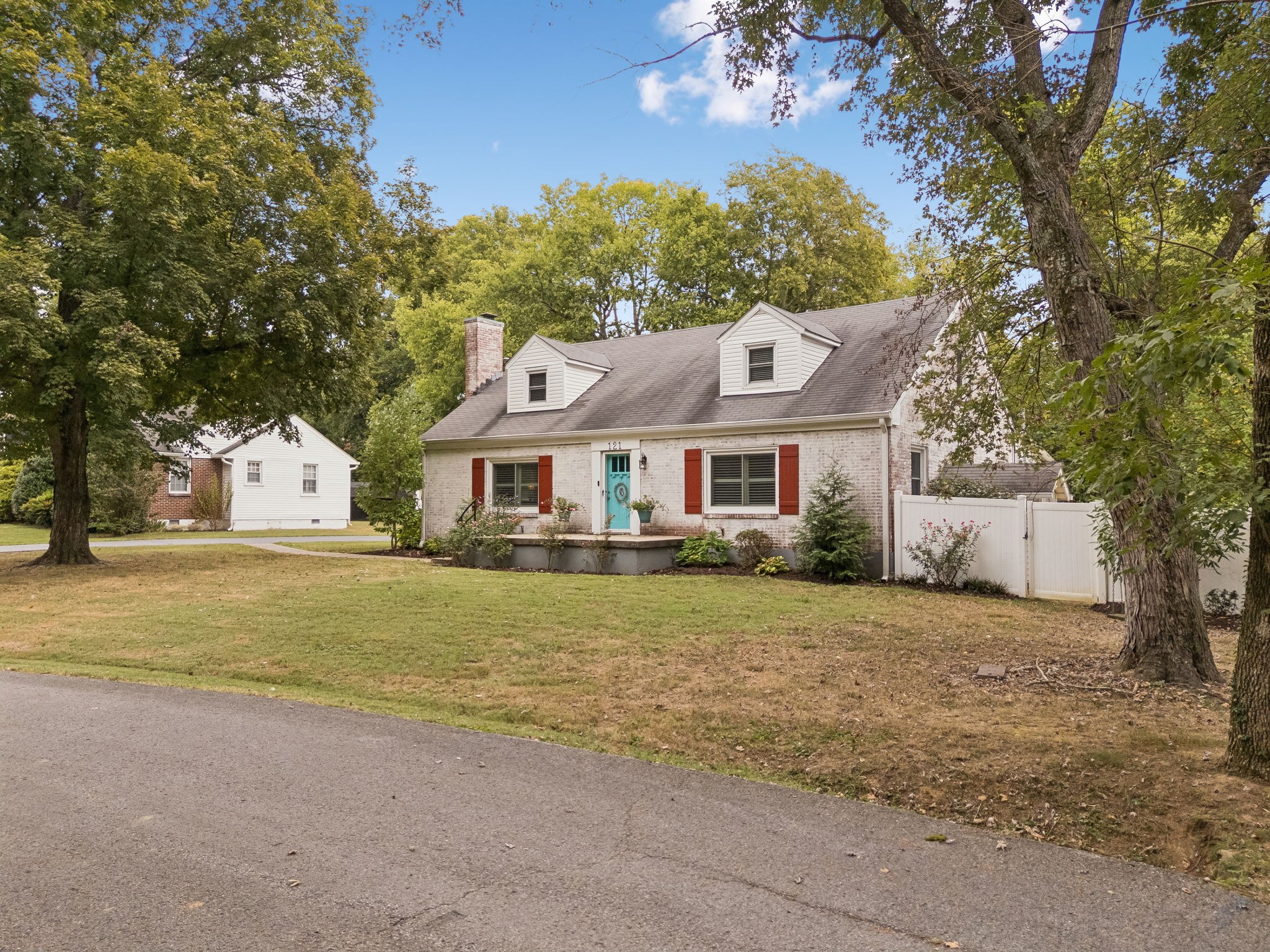 Brick house with dormers, red shutters, and a turquoise front door, framed by mature trees.