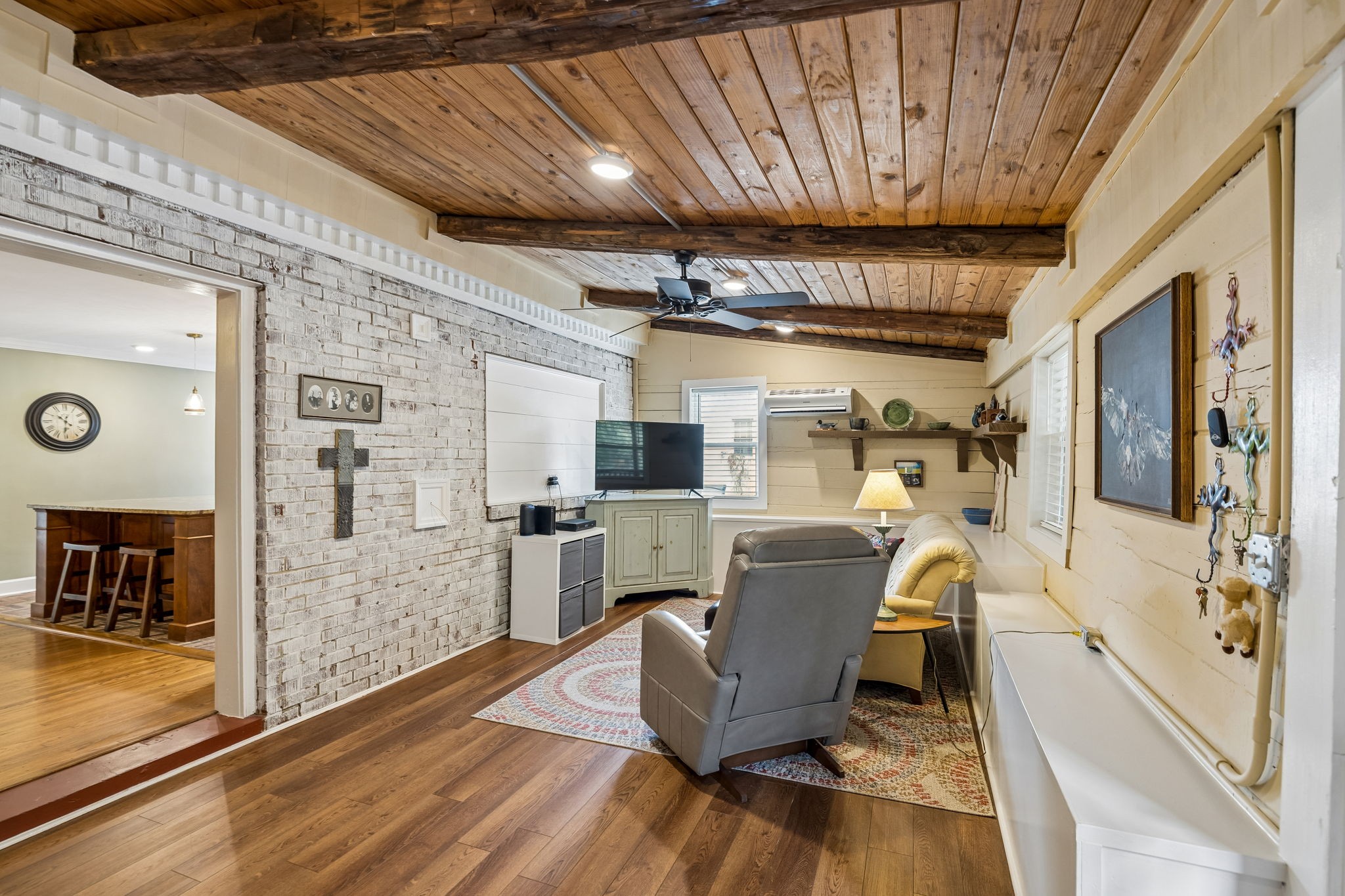 Living room with a wood-plank ceiling, exposed beams, whitewashed brick wall, and gray seating.