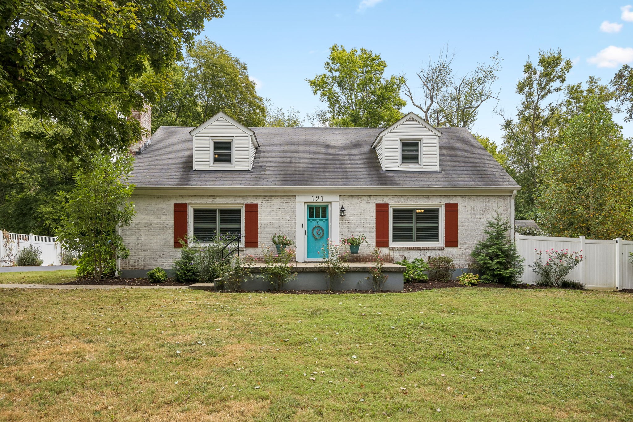 White brick house with two dormers, red shutters, and a turquoise front door marked 121.