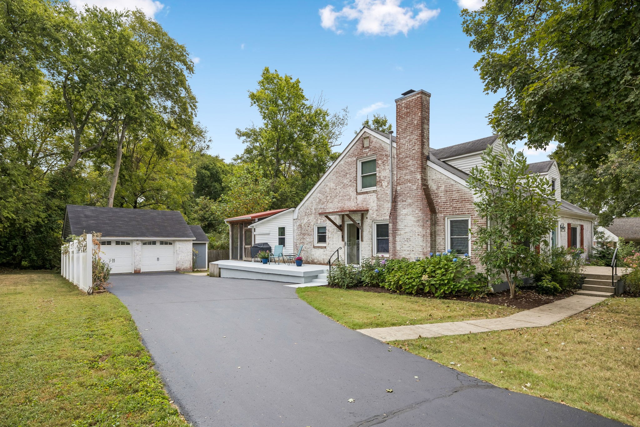Whitewashed brick house with a tall chimney, covered patio, and detached garage beside the driveway.
