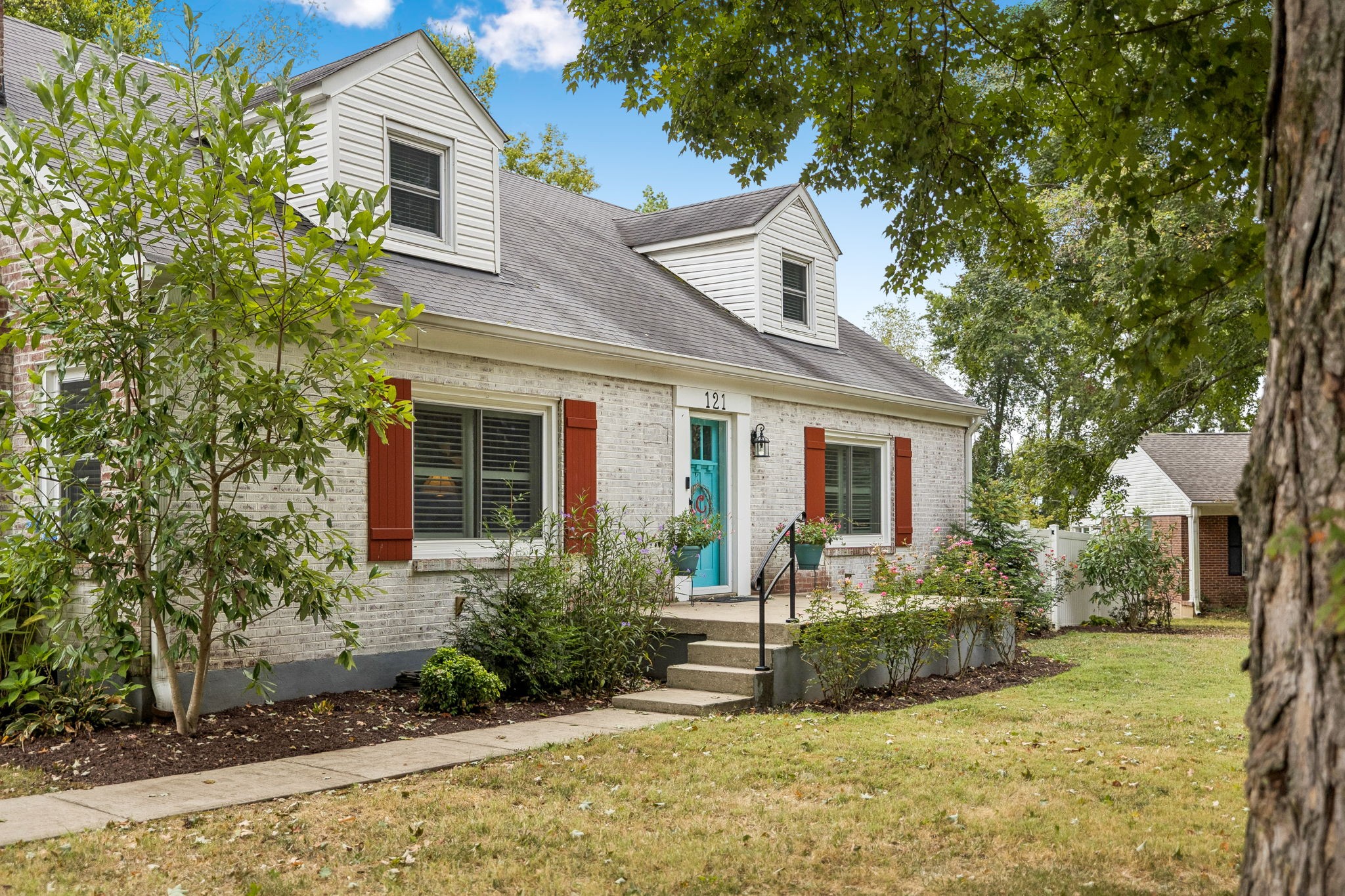 Light brick house with two dormers, red shutters, and a turquoise front door.