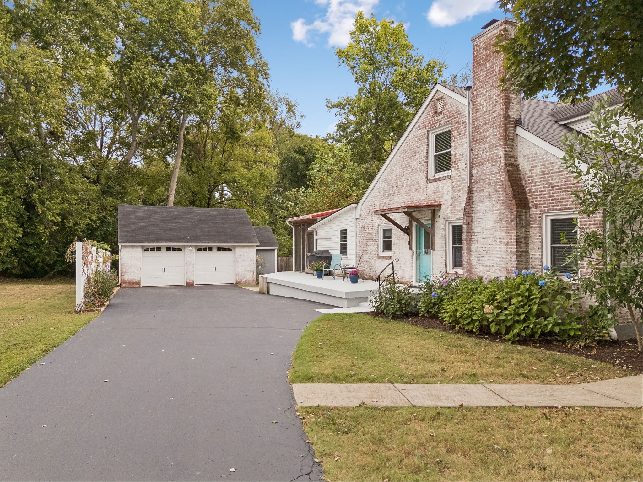 Brick house with a turquoise door, raised patio, flowering shrubs, and detached two-car garage.