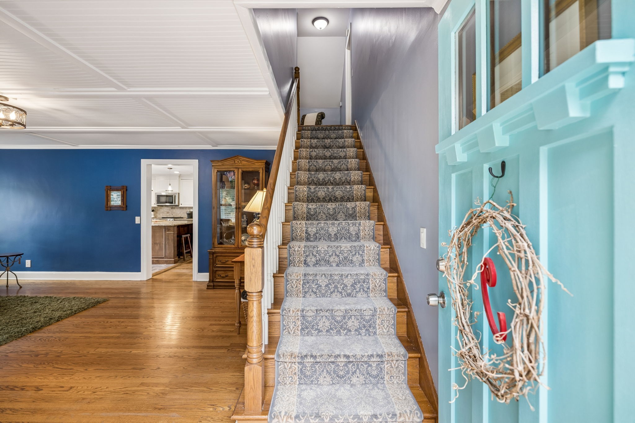 Entryway with a carpeted staircase, blue walls, hardwood floors, and an open turquoise front door.