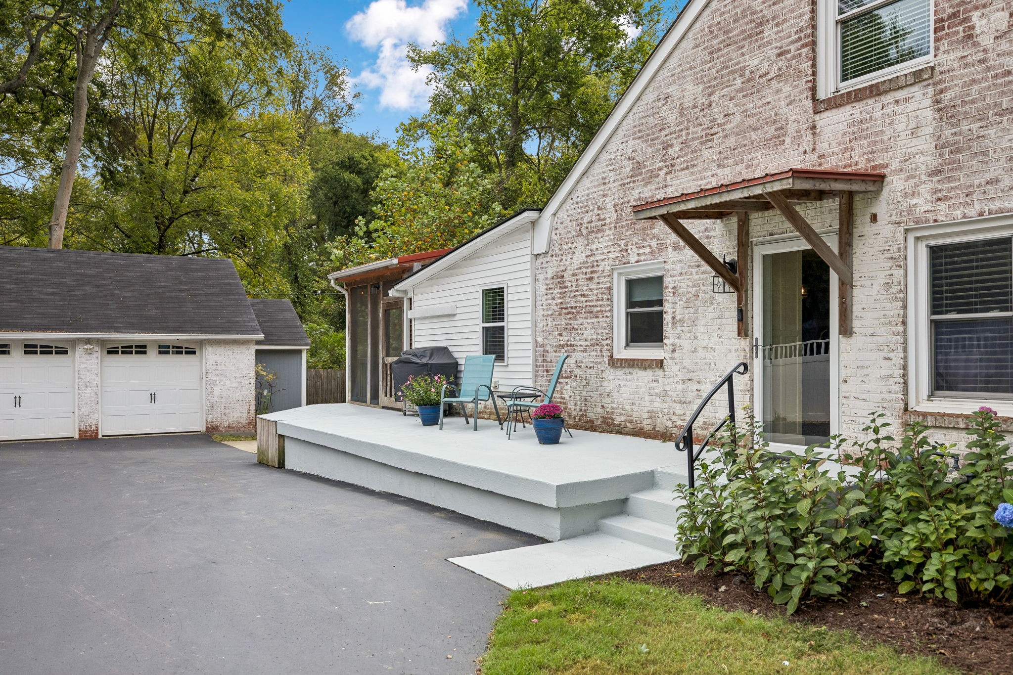 Whitewashed brick home with raised patio, back-door awning, detached garage, and paved driveway.