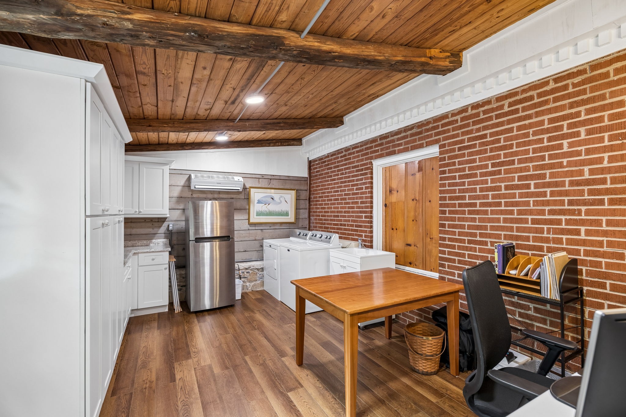 Laundry room with white washer and dryer, red brick wall, and exposed wood-beam ceiling.