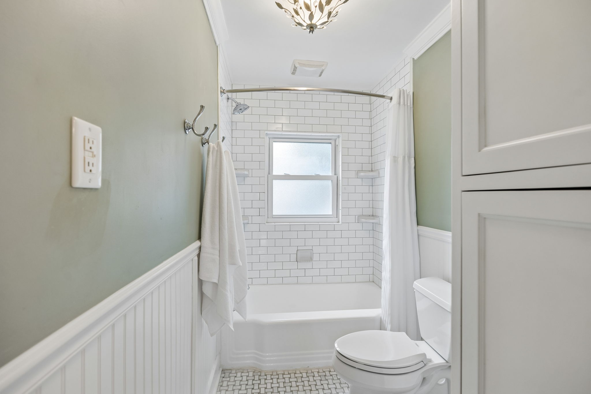 Bathroom with a subway-tile tub and shower, frosted window, and white beadboard wainscoting.