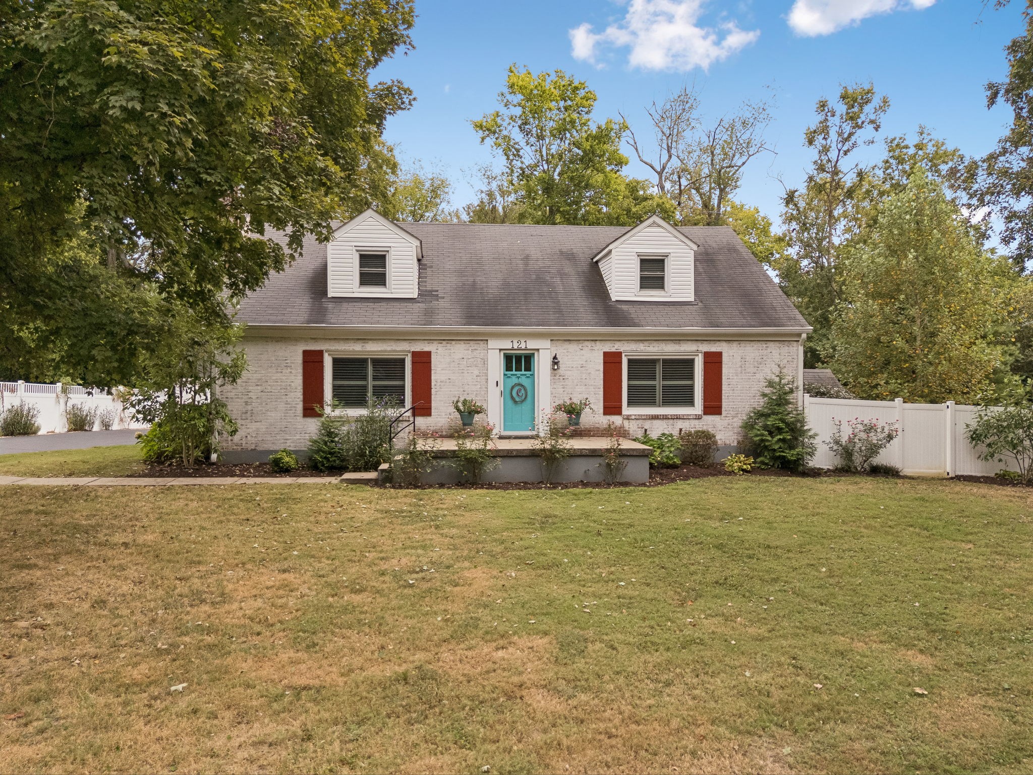 Light brick house with two dormers, red shutters, turquoise front door, and a broad front lawn.