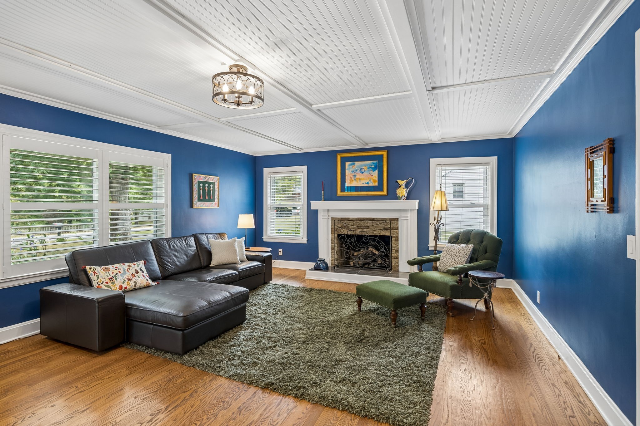 Living room with a stone fireplace, blue walls, black leather sectional, and hardwood floors.