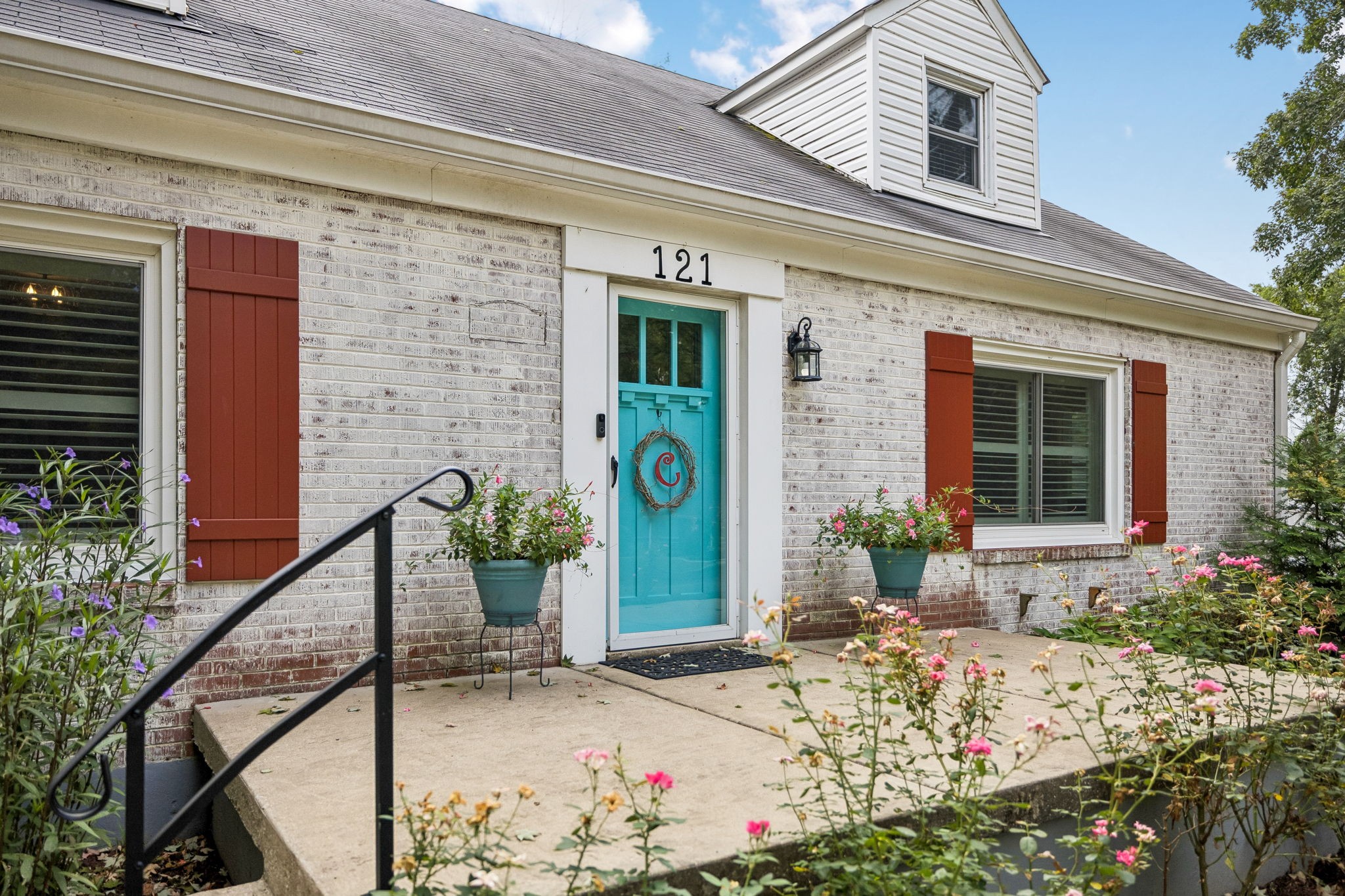 Home entrance with a turquoise door, red shutters, and flowering garden beds.