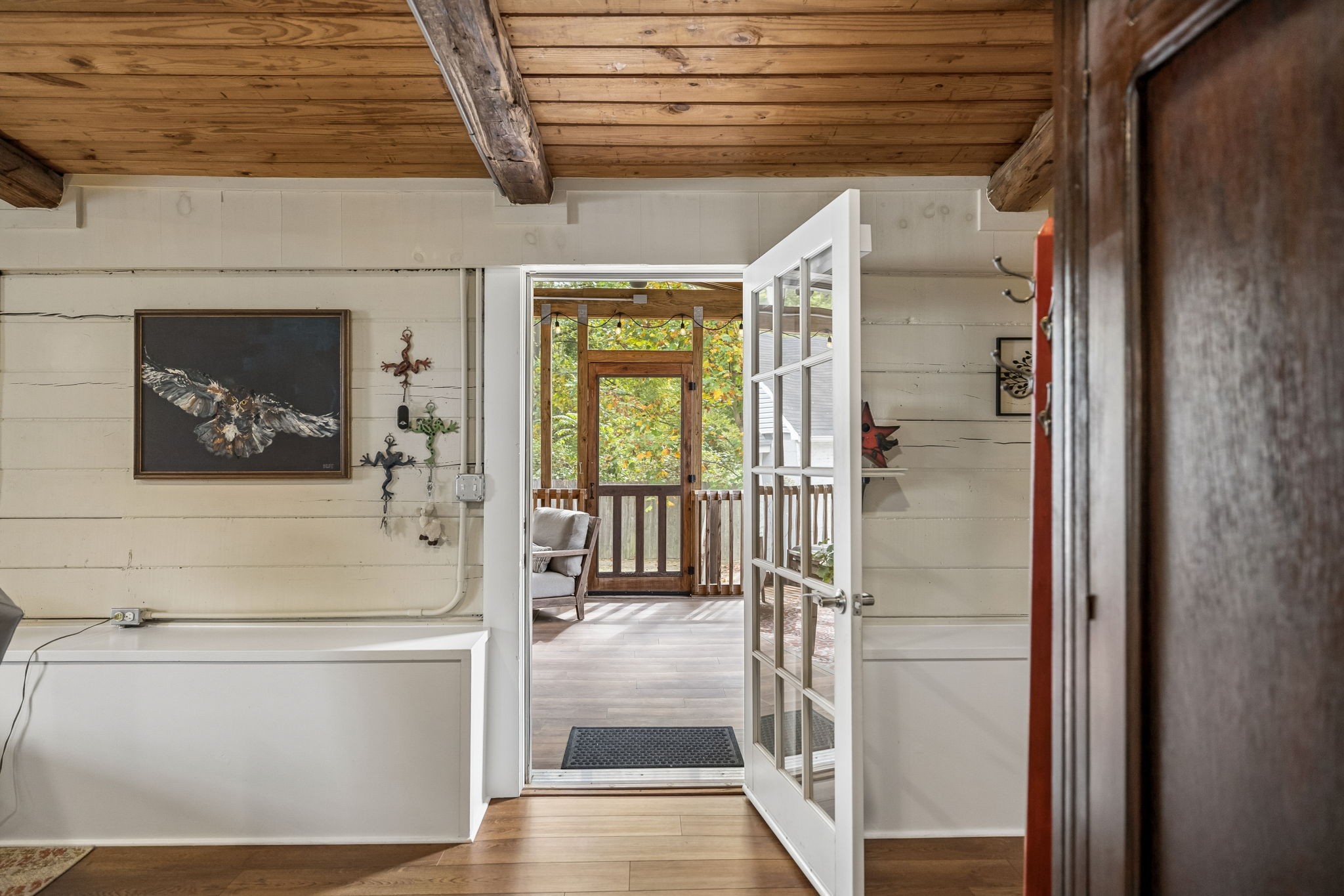 Entryway with exposed wood beams and an open glass-paneled door to a covered porch