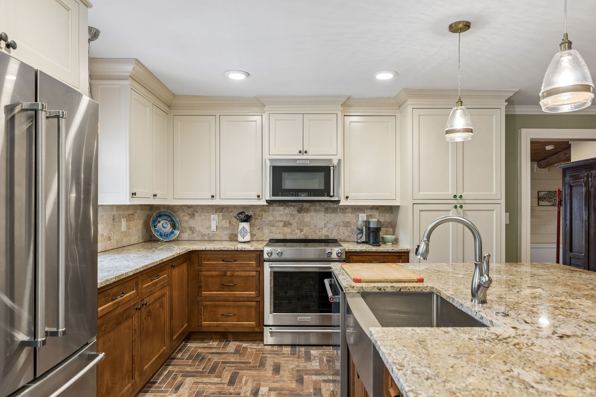 Kitchen with cream cabinets, warm wood drawers, stainless steel appliances, and a granite island with sink.