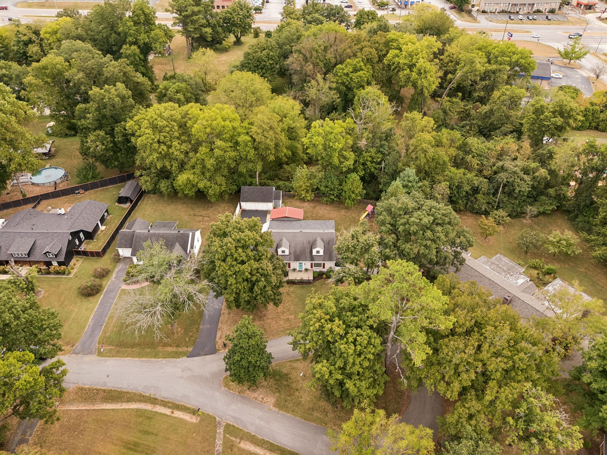Aerial view of a light-colored house with red shutters, a broad lawn, and dense trees behind it.