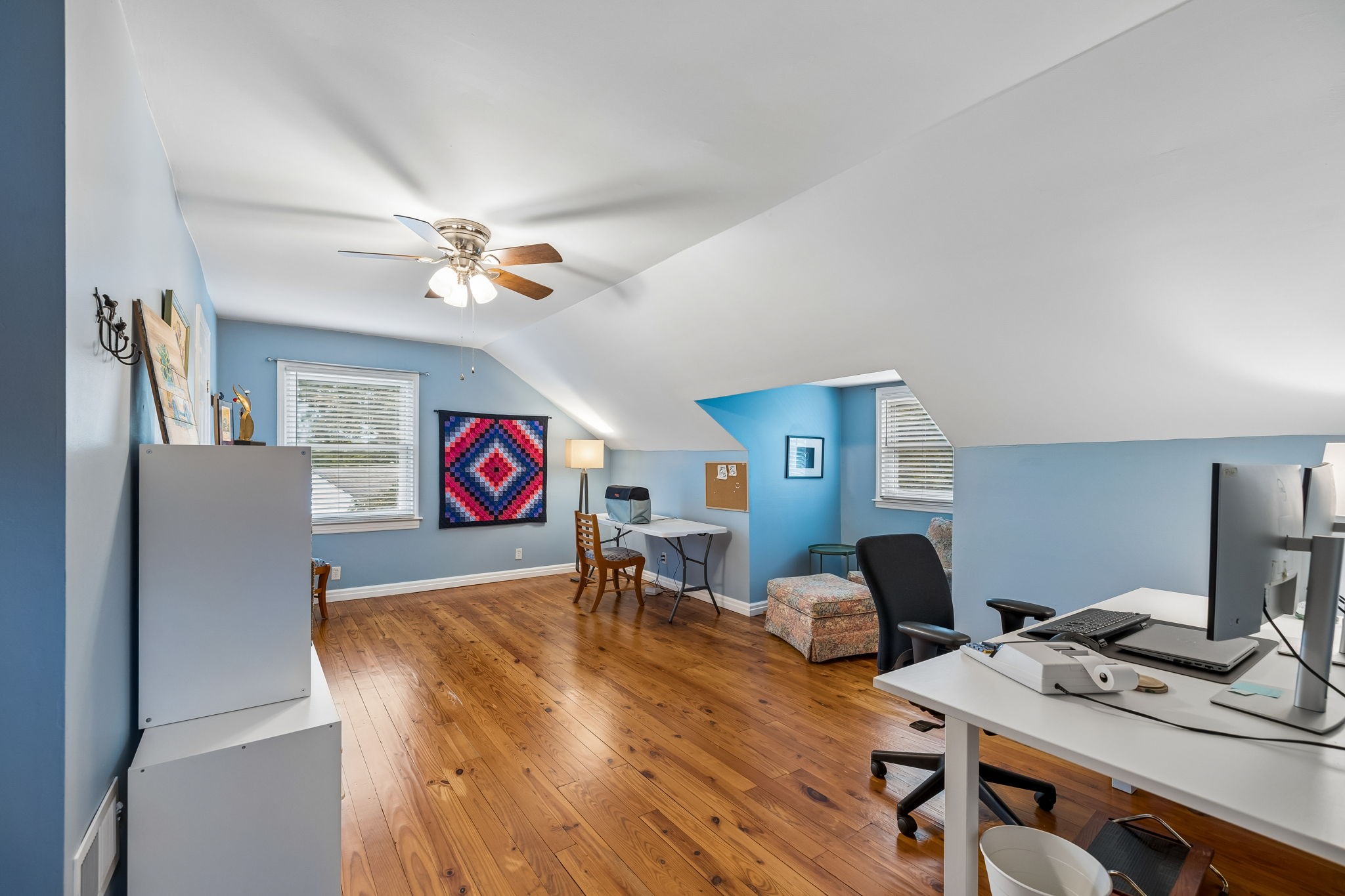 Upstairs home office with blue walls, sloped ceilings, hardwood floors, and two workstations.