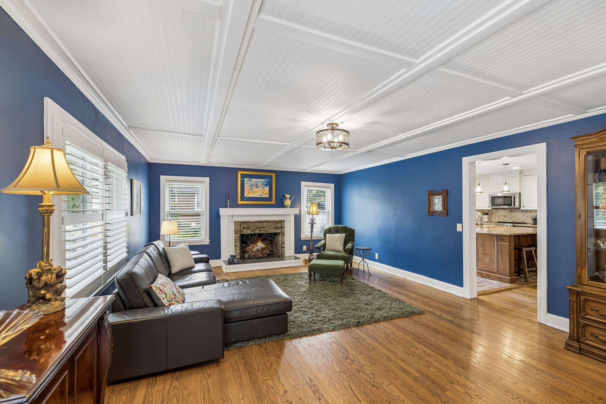 Blue living room with a stone fireplace, leather sectional, green armchair, and hardwood floors.