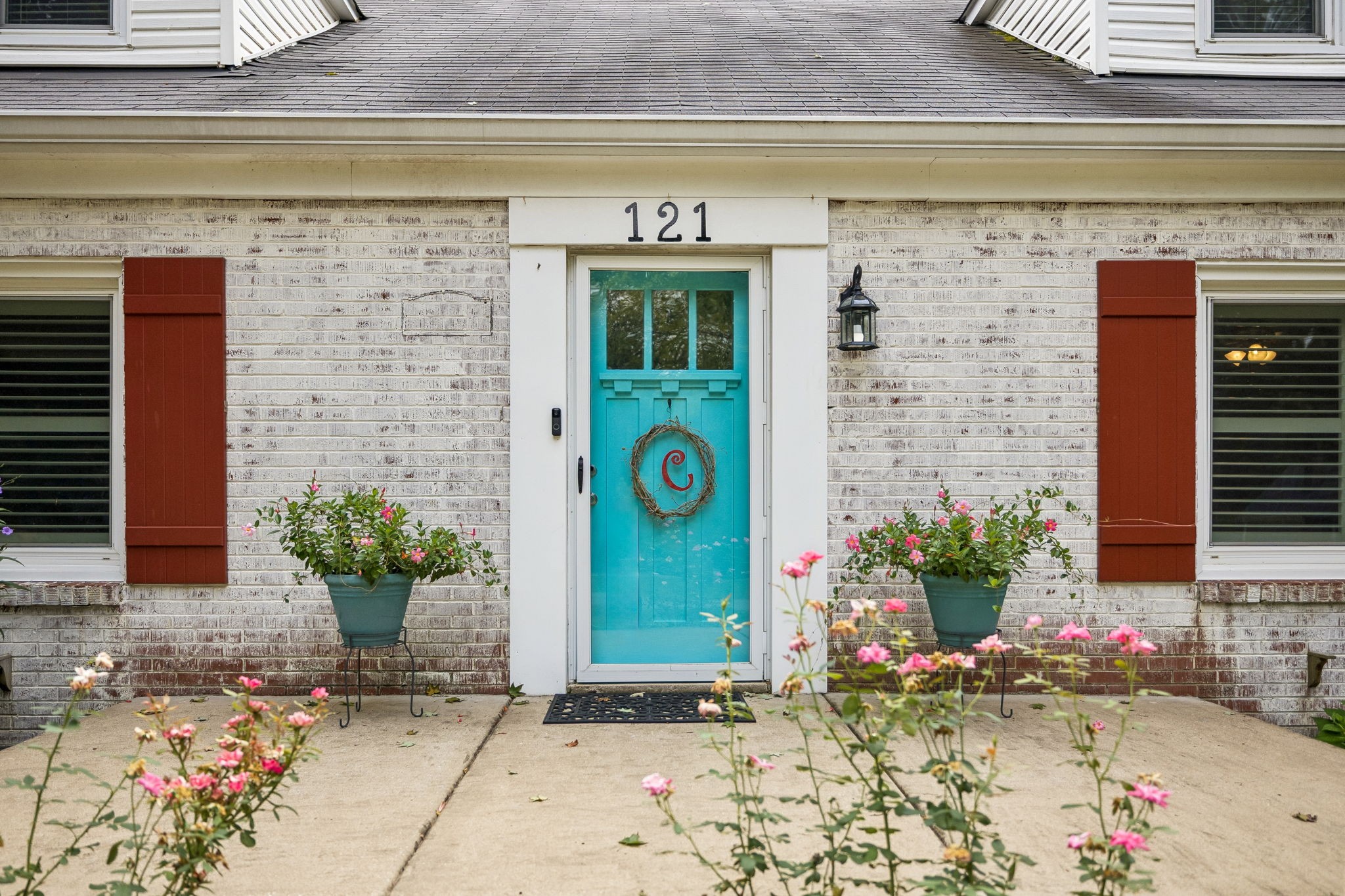 Home entrance with a turquoise door, whitewashed brick, red shutters, and pink flowers.