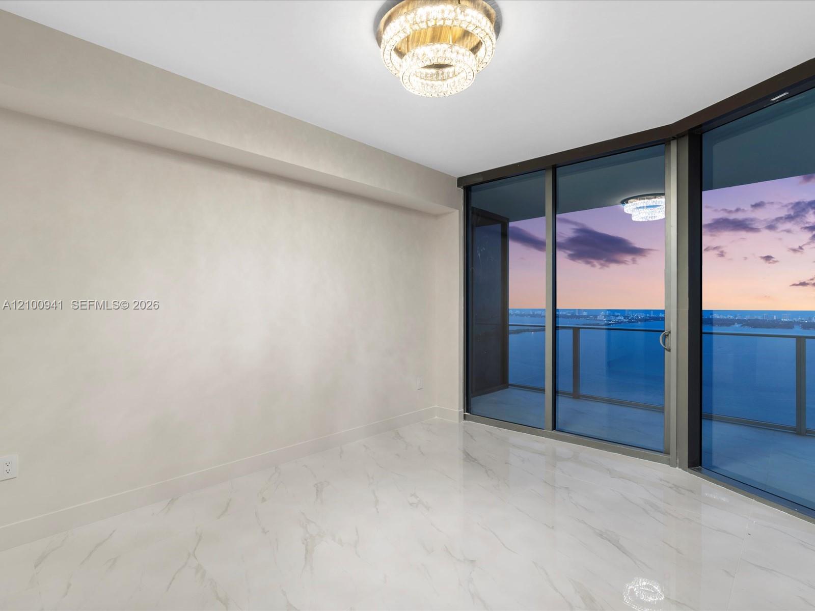 Empty high-rise room with marble floors, a crystal chandelier, and dusk views across the water.