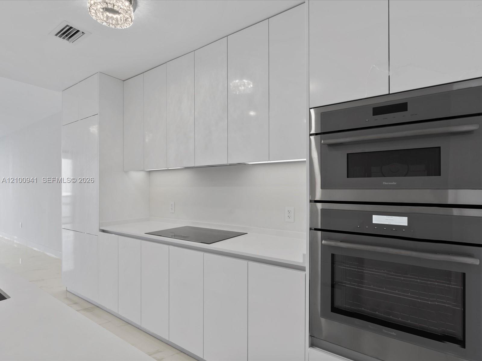 Modern white kitchen with glossy cabinets, induction cooktop, and stainless steel double wall ovens.