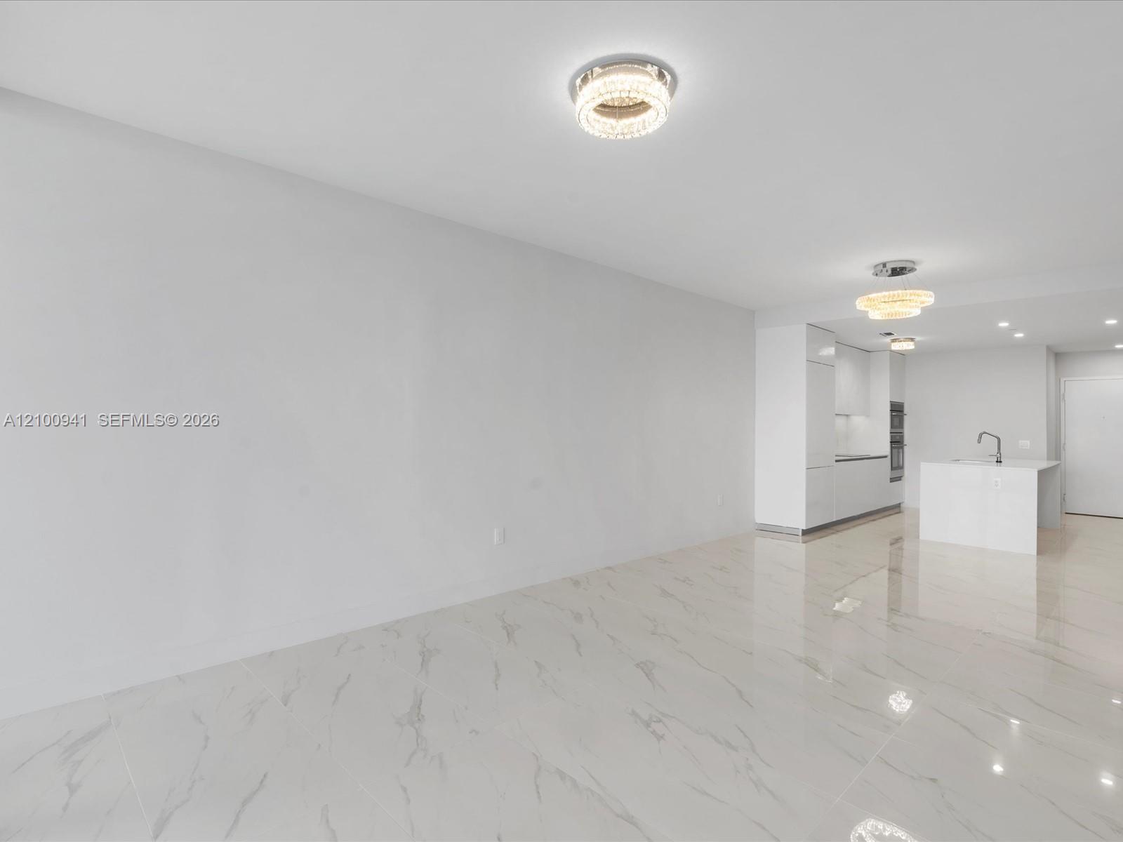 Empty open-plan living area with glossy marble-look floors, a white kitchen island, and crystal ceiling lights.