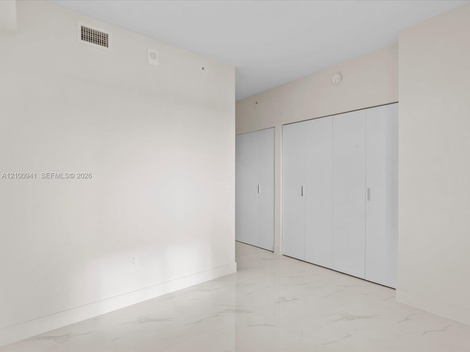 Vacant hallway with white closet doors and glossy marble-look flooring.