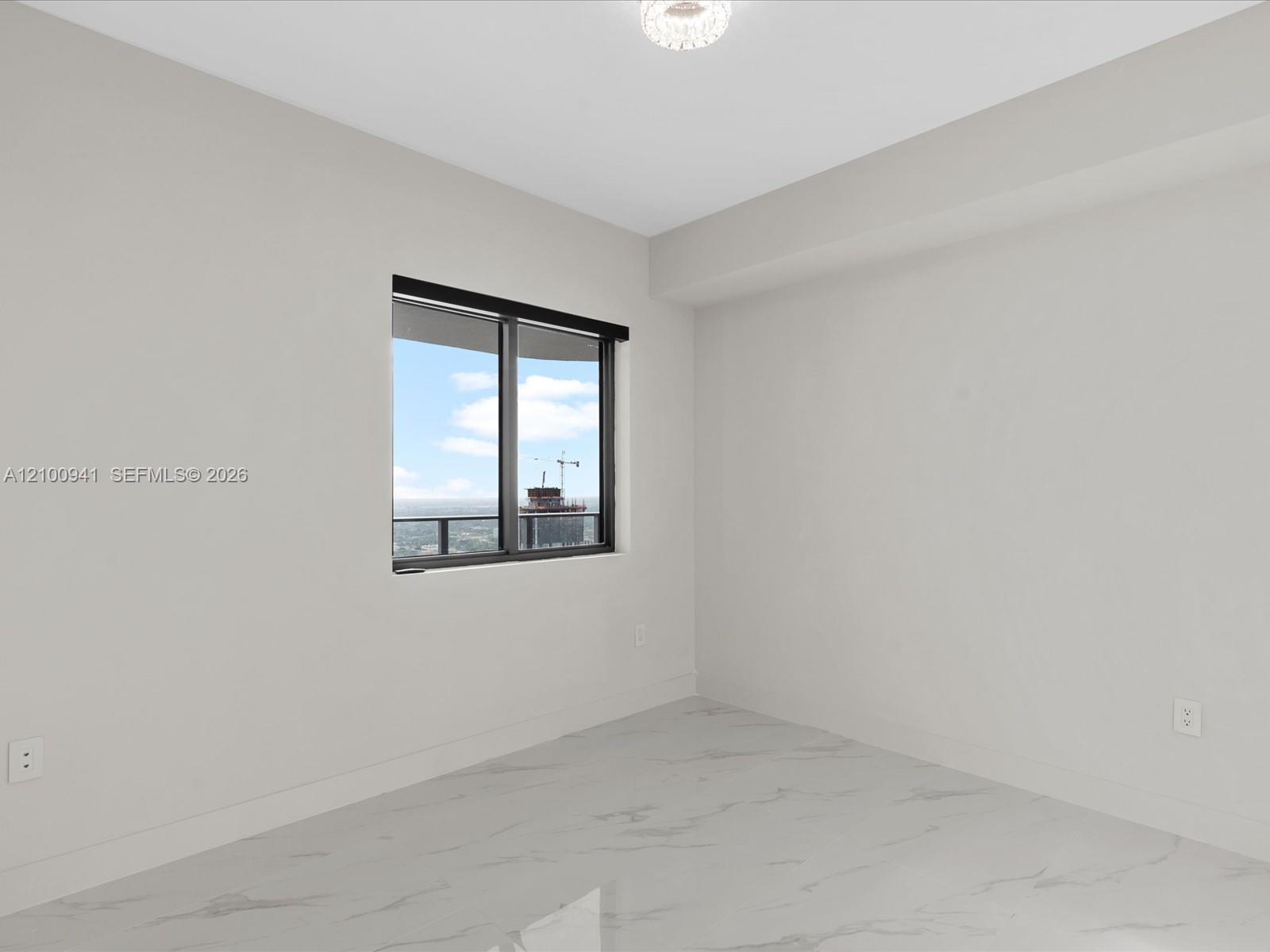 Empty room with marble-patterned floors and a large window overlooking water and a building under construction.