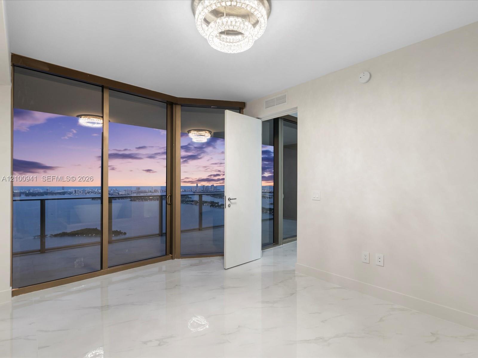 Empty condo interior with floor-to-ceiling windows overlooking water and the city at dusk.
