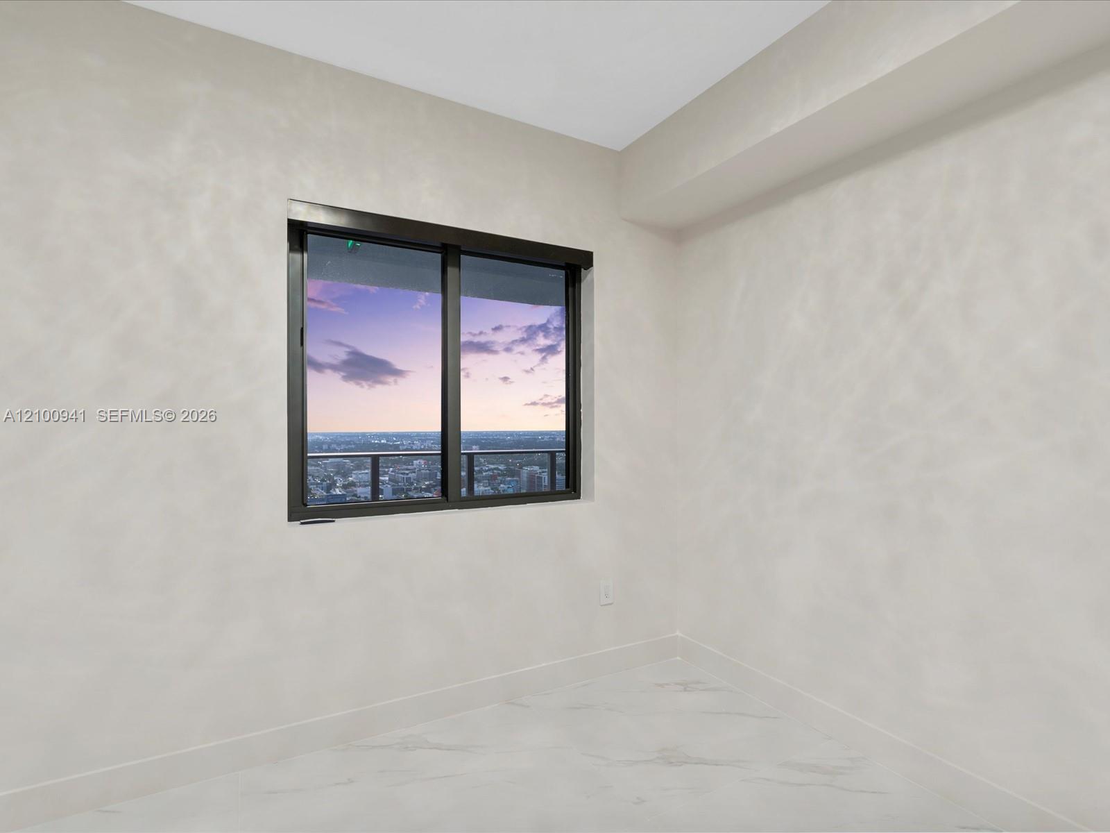 Empty white room with marble-look tile and a window overlooking the city at dusk.