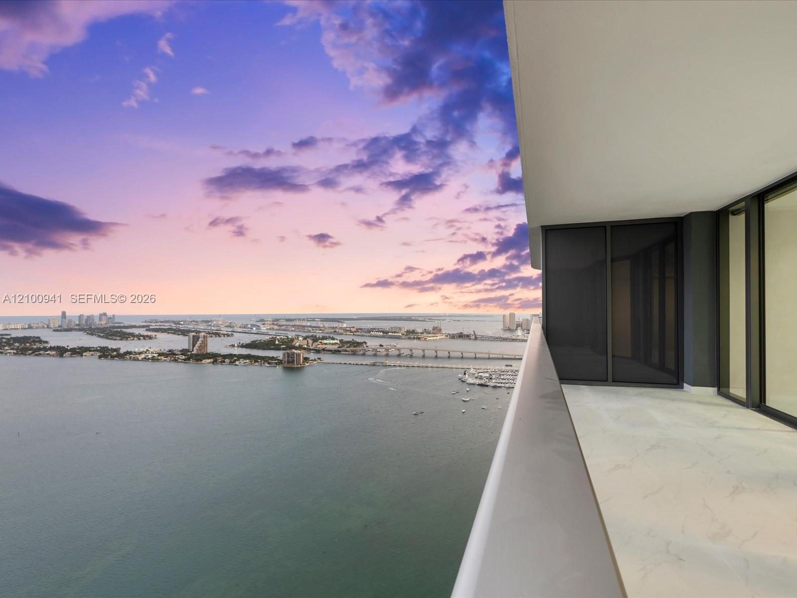 High-rise condo balcony overlooking Biscayne Bay, bridges, boats, and the Miami skyline at dusk.