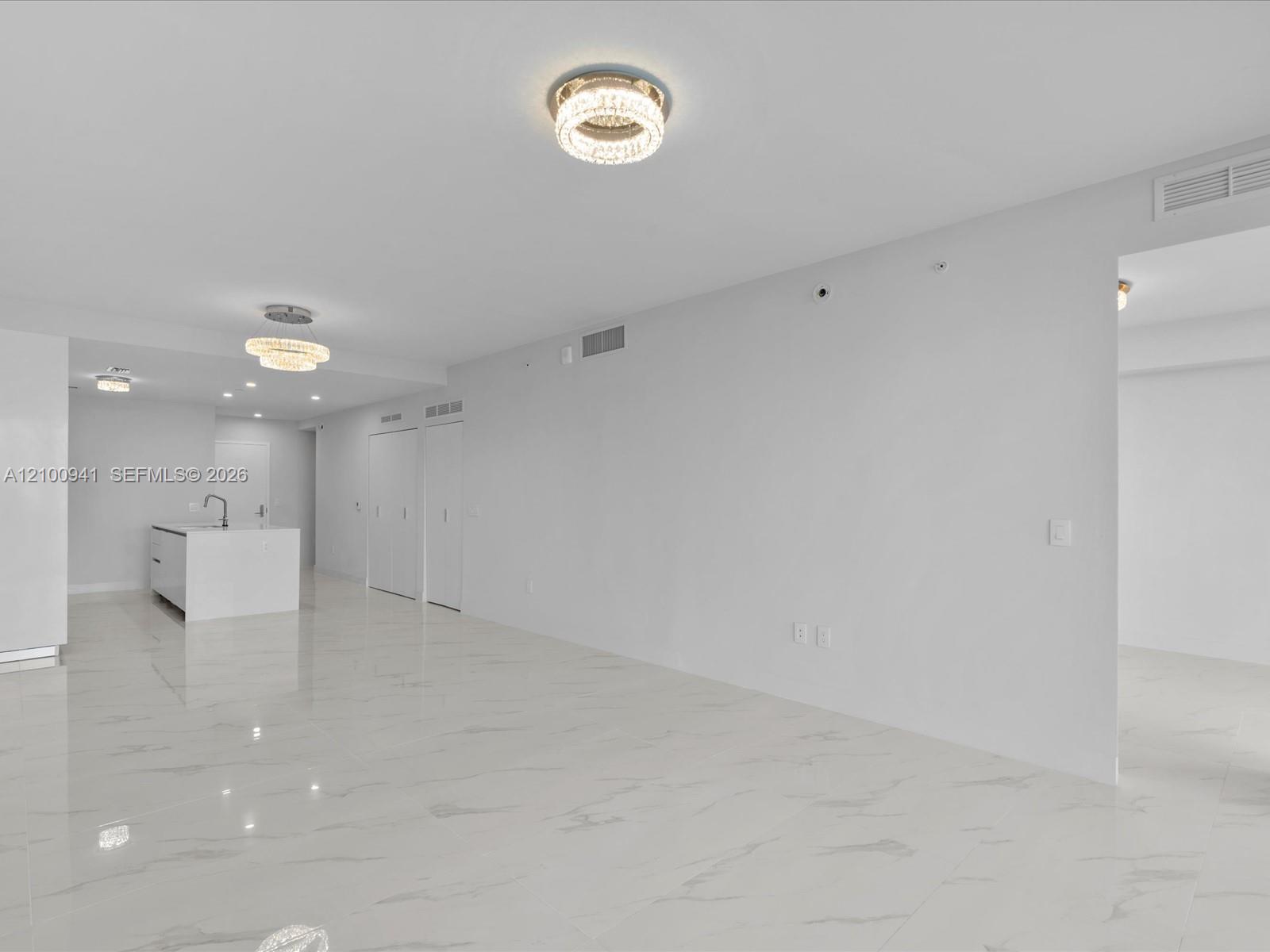 Open-plan living area with glossy veined tile floors, crystal ceiling lights, and a kitchen island.