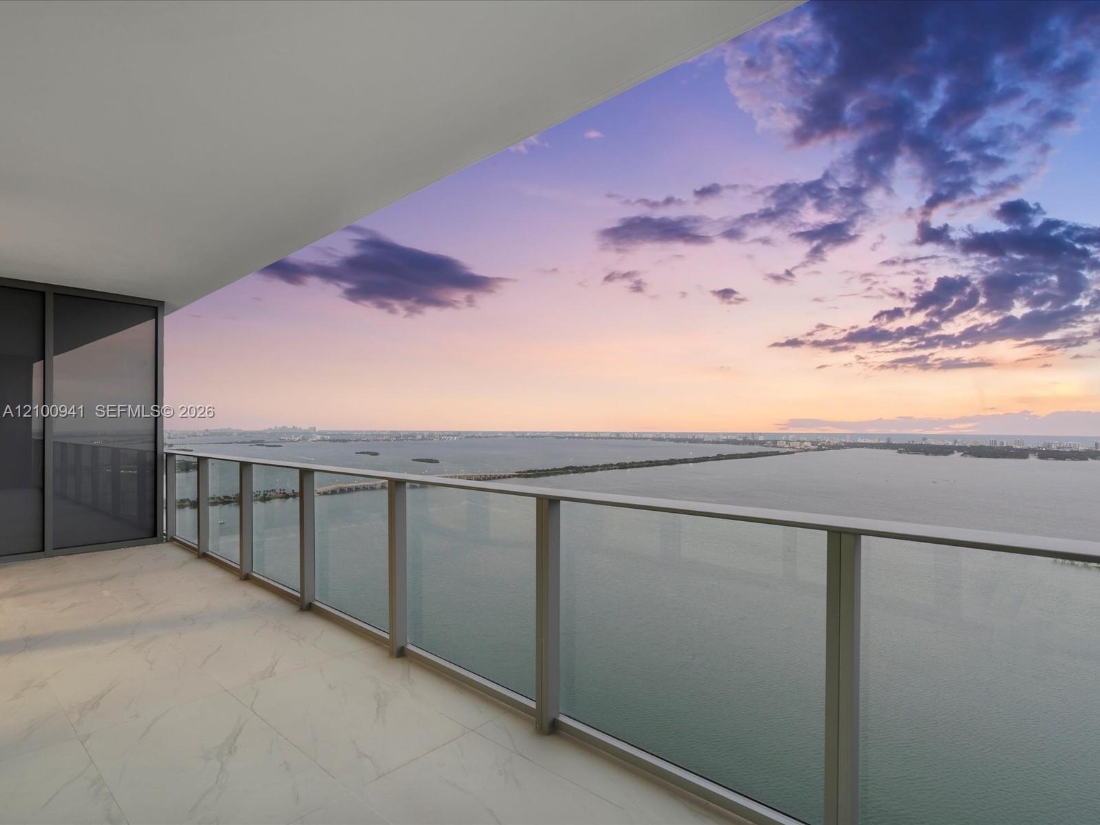 High-rise balcony overlooking the bay and distant skyline beneath a pink and purple dusk sky.