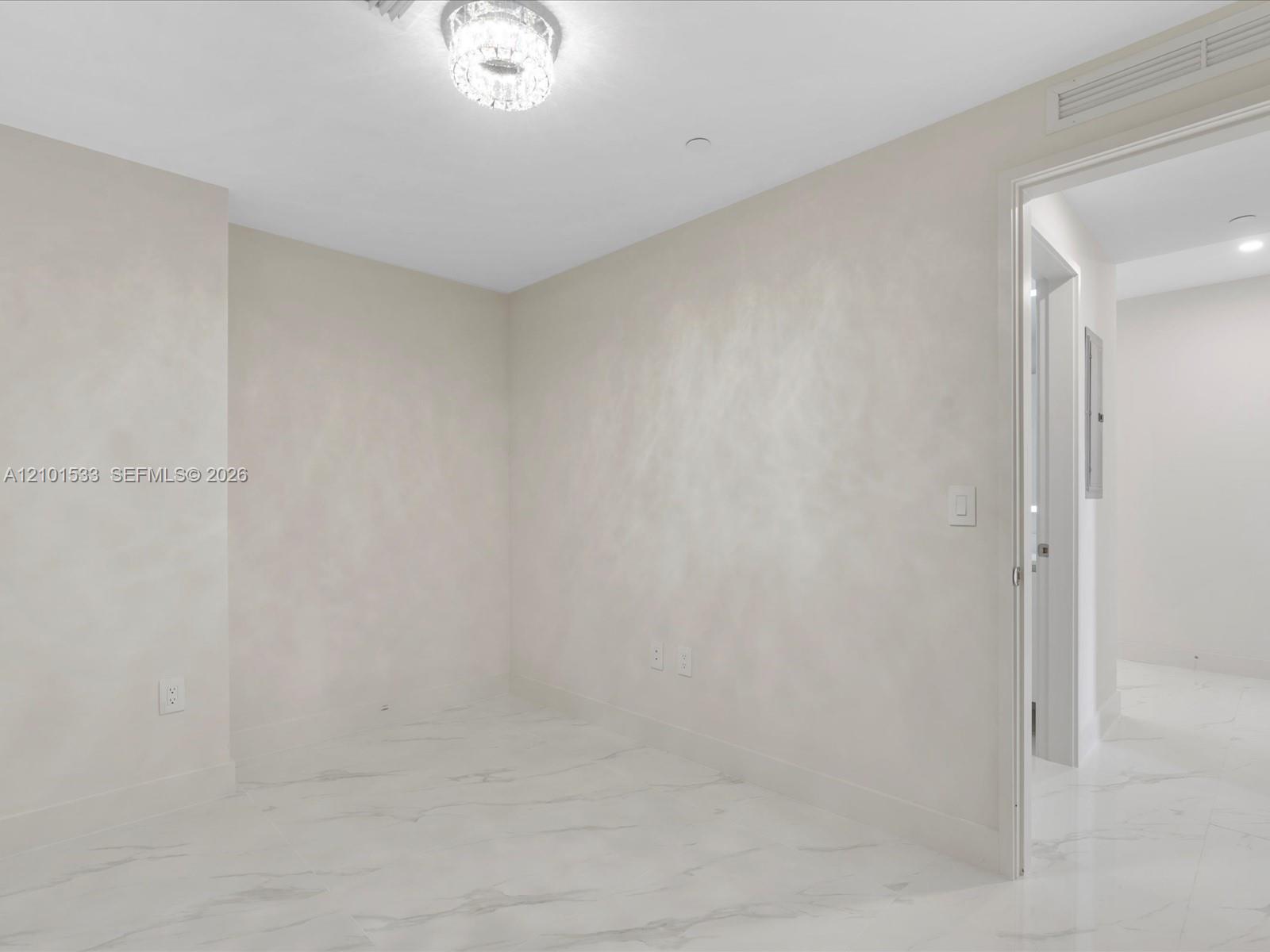 Empty white room with glossy marble-look tile floors and a crystal chandelier.