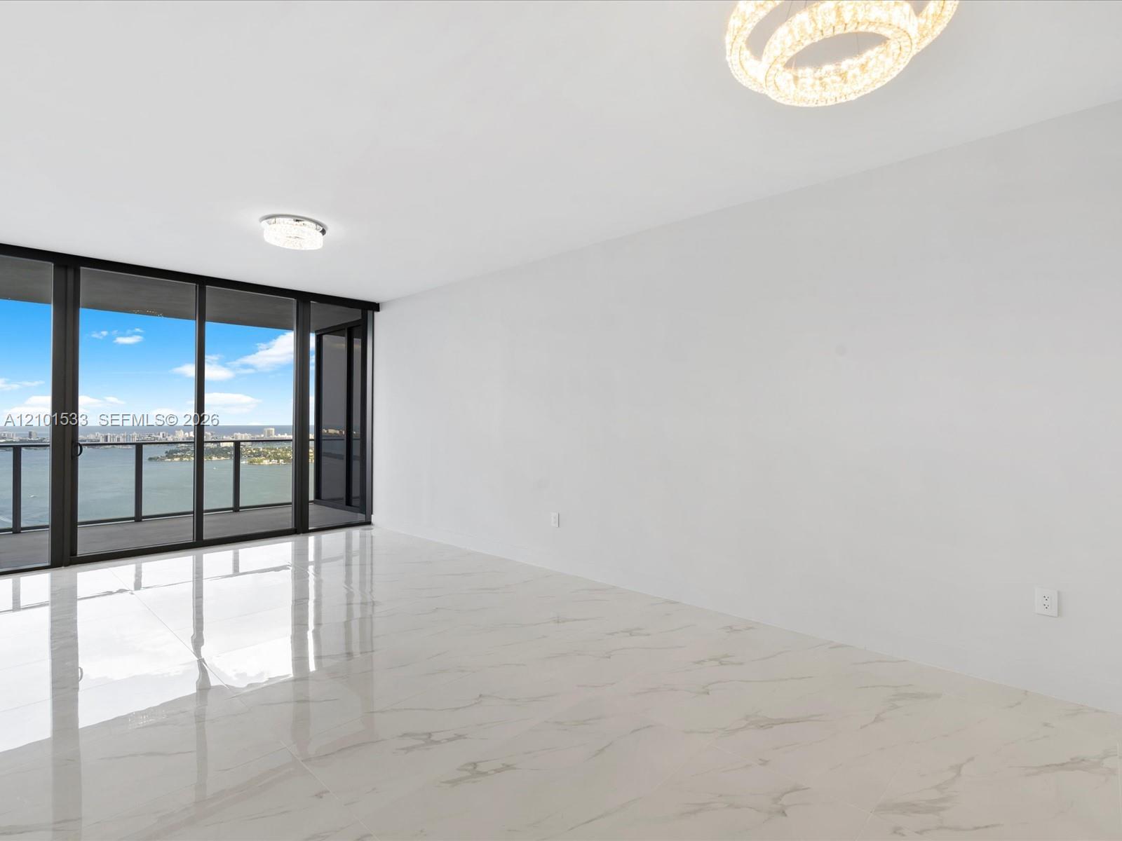 Vacant condo living area with glossy white floors and glass doors overlooking the water and city skyline.