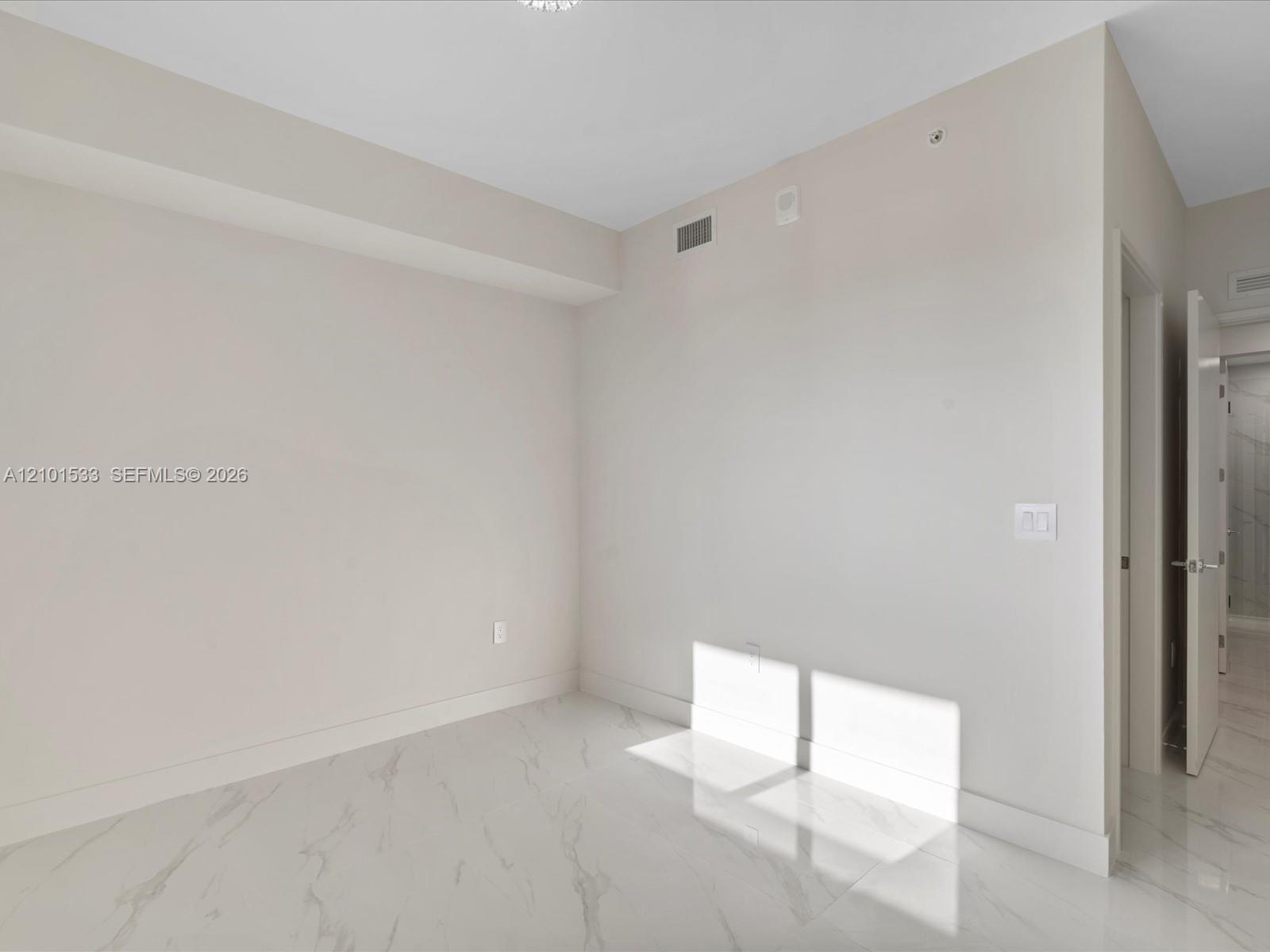 Empty bright room with glossy marble-look floors and sunlight streaming through the doorway.