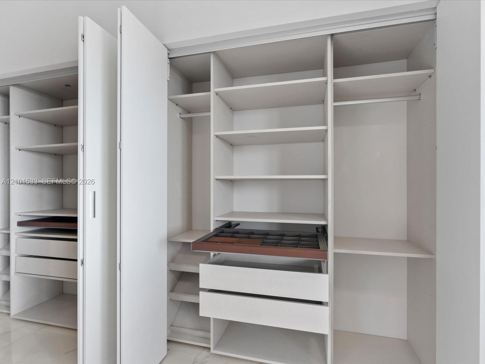 Walk-in closet with white built-in shelves and open drawers with a divided organizer tray.