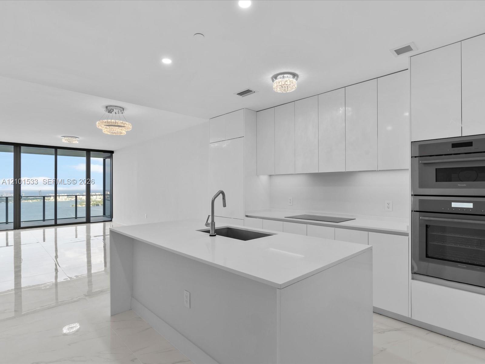 Modern white kitchen with a large island and sliding doors overlooking the water.