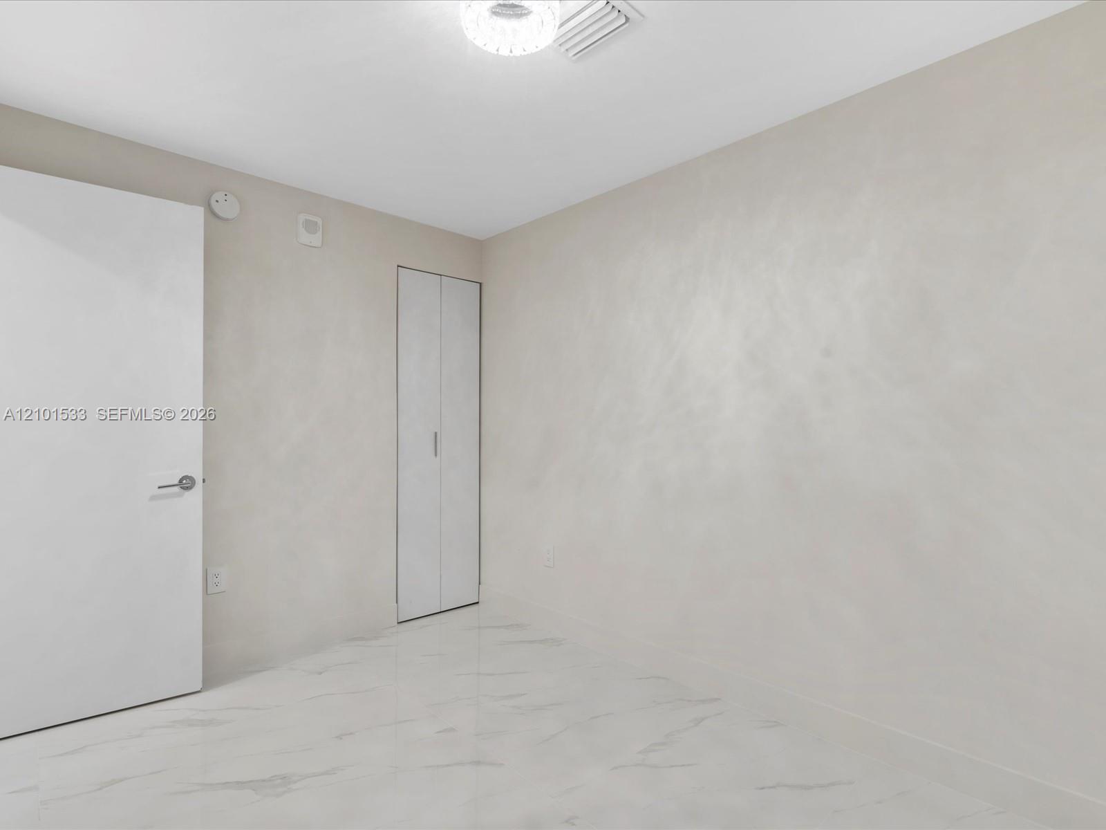 Empty room with a built-in closet and glossy marble-look tile floor.