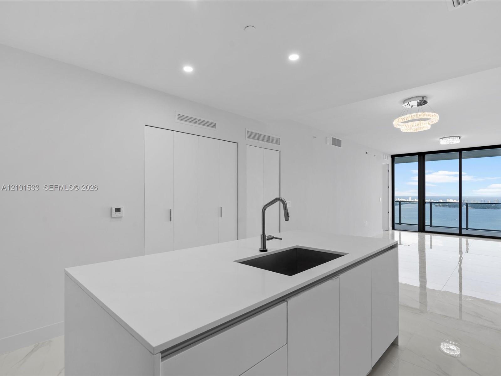 Modern white kitchen with a large island and water views through floor-to-ceiling windows.