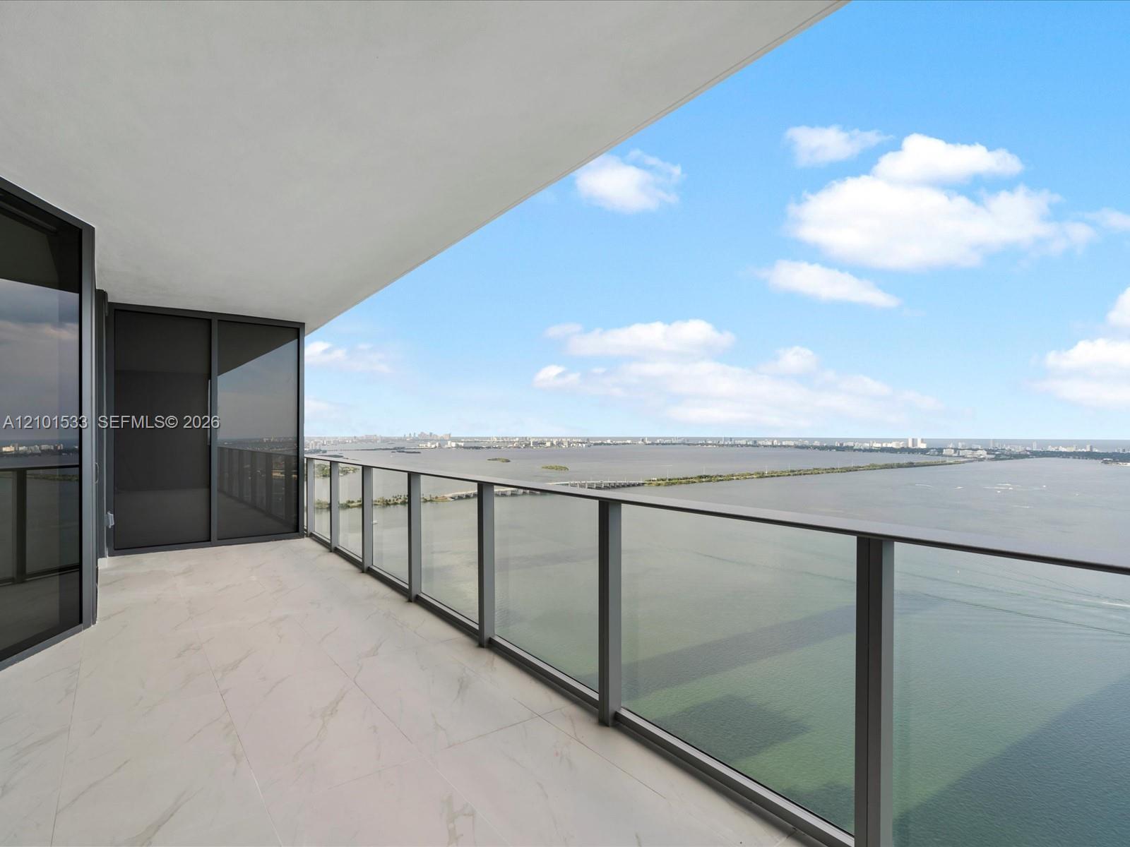 Condo balcony with glass railing overlooking the bay and distant Miami skyline.