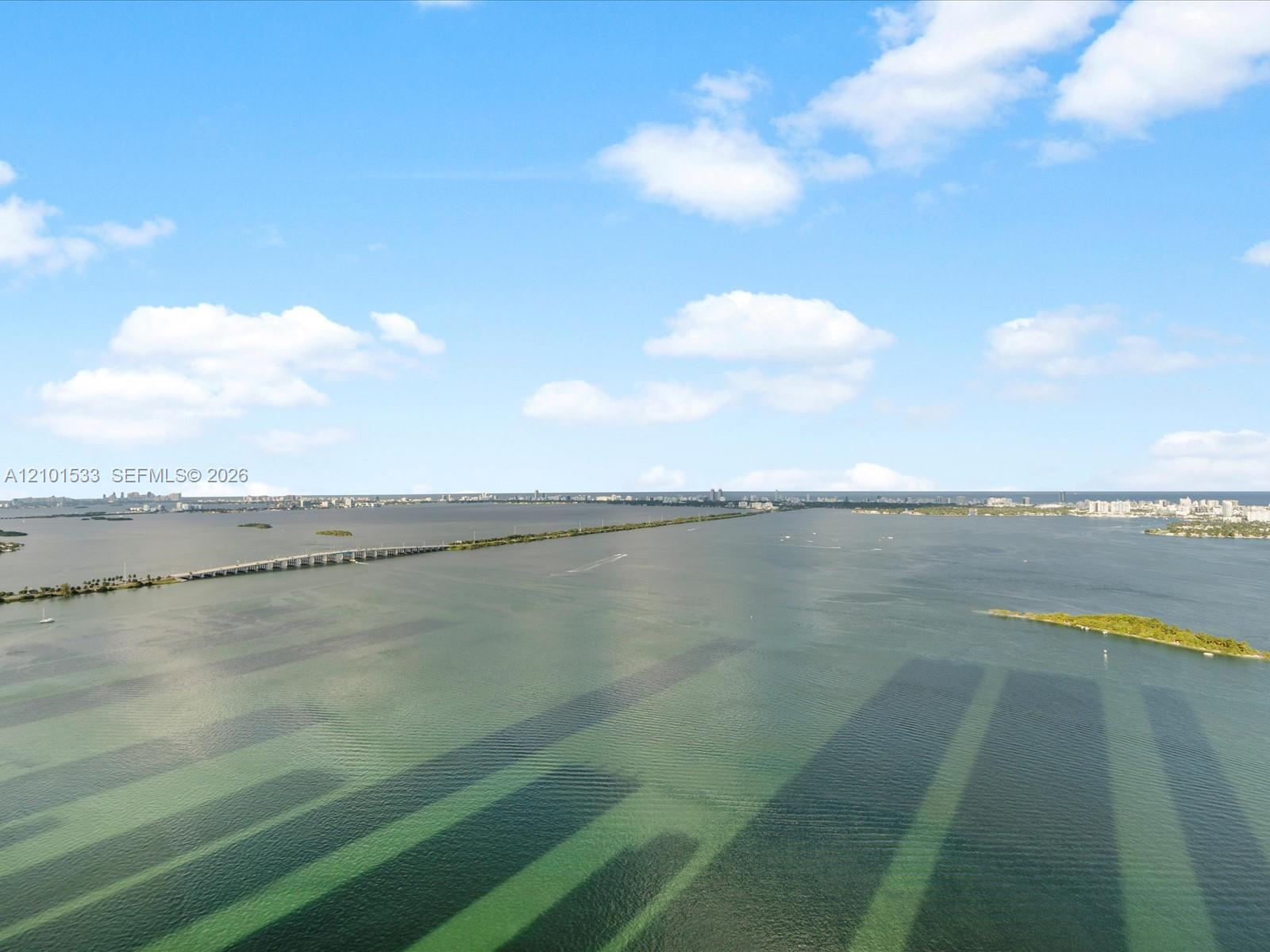 Aerial bay view with a causeway, small islands, and distant Miami buildings.