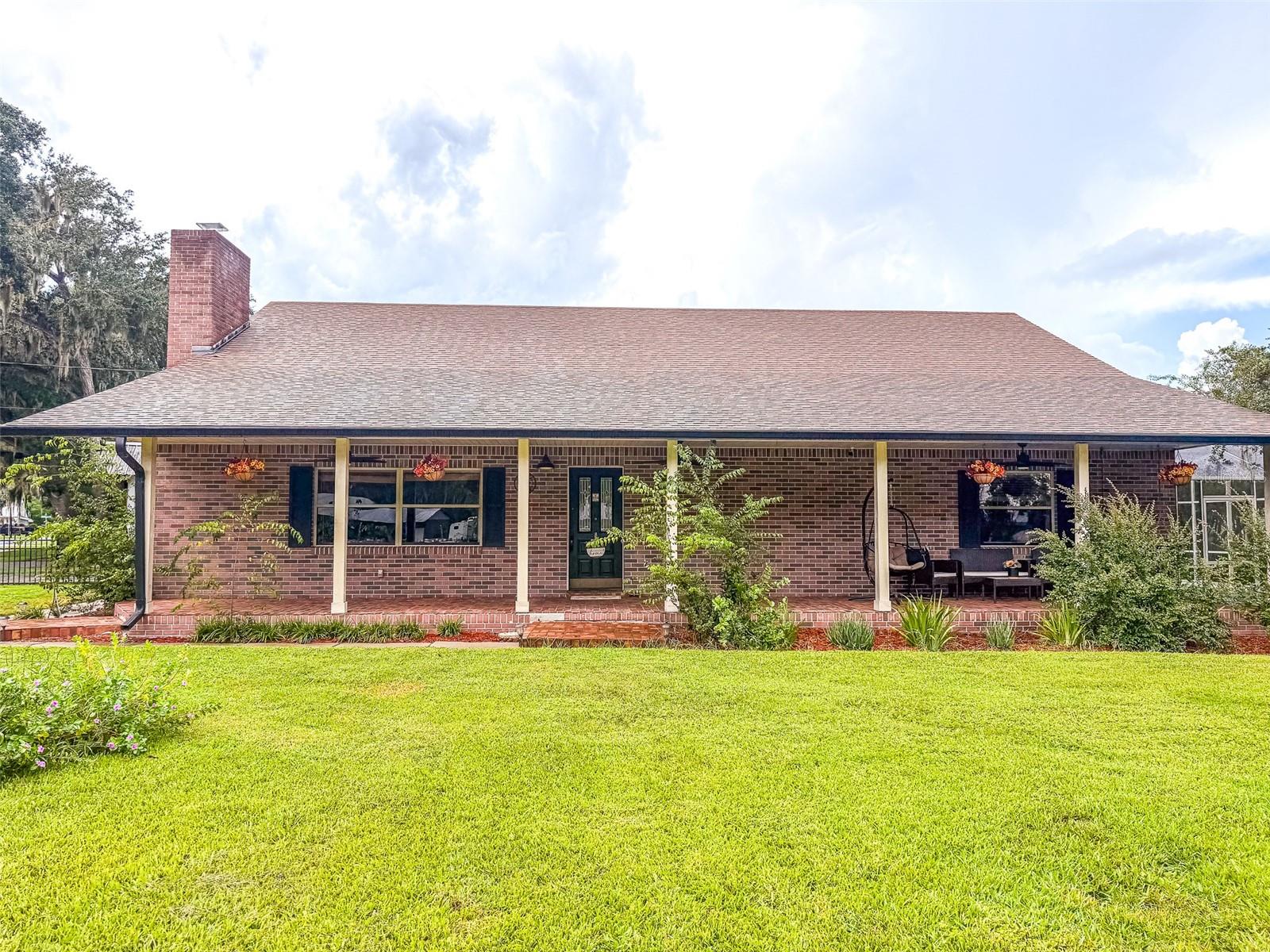 Brick ranch-style home with a covered porch, outdoor seating, and a broad front lawn.