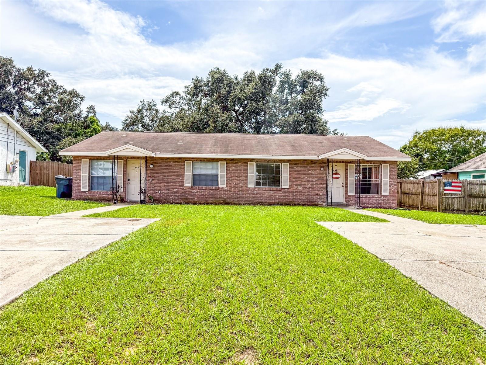Red-brick duplex with two separate entrances, concrete driveways, and a broad front lawn.