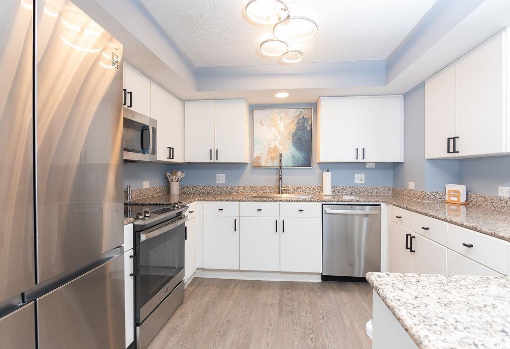Renovated kitchen with white cabinets, granite counters, stainless steel appliances, and light wood-look flooring.