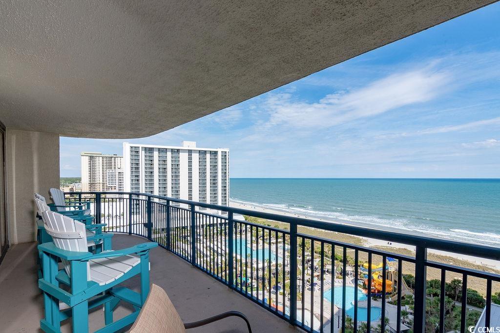 Condominium balcony with turquoise chairs overlooking the ocean, beach, pool, and nearby towers.