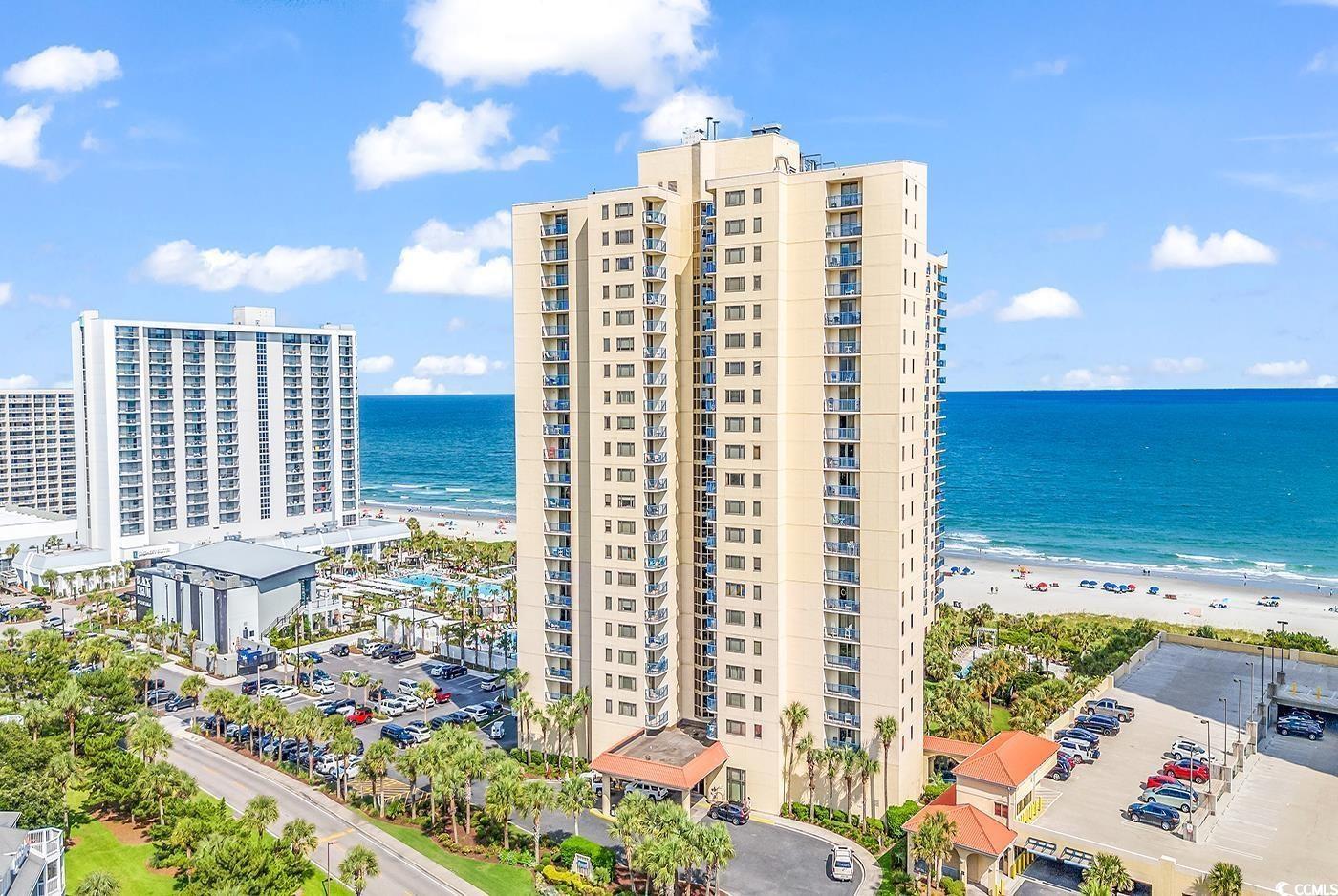 Beachfront condominium tower beside the ocean, with balconies and neighboring high-rises.
