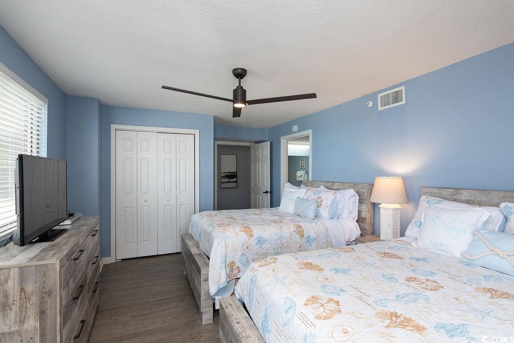 Bedroom with two patterned beds, blue walls, a ceiling fan, and a dresser with television.